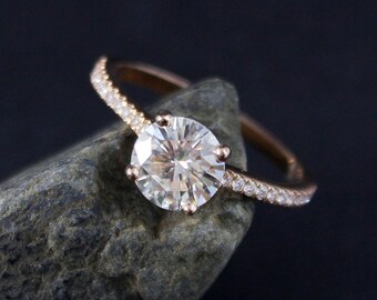 Könnte beinhalten: Ein Verlobungsring aus Roségold mit einem runden Diamanten in der Mitte und einer Reihe kleinerer Diamanten.