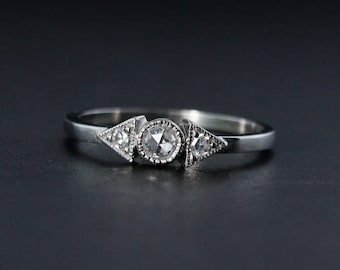 Può includere: Un anello d'argento con tre diamanti. Il diamante centrale è rotondo e i due diamanti laterali sono triangolari.