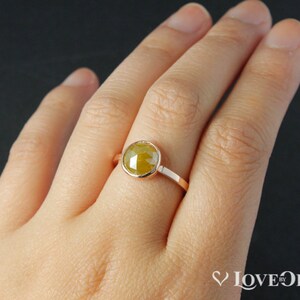 Puede incluir: Un anillo de oro con una piedra preciosa amarilla engastada en un engaste de bisel. El anillo est&aacute; en el dedo de una persona.
