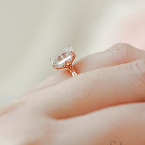 May include: A rose gold engagement ring with a large, clear, square-shaped diamond.