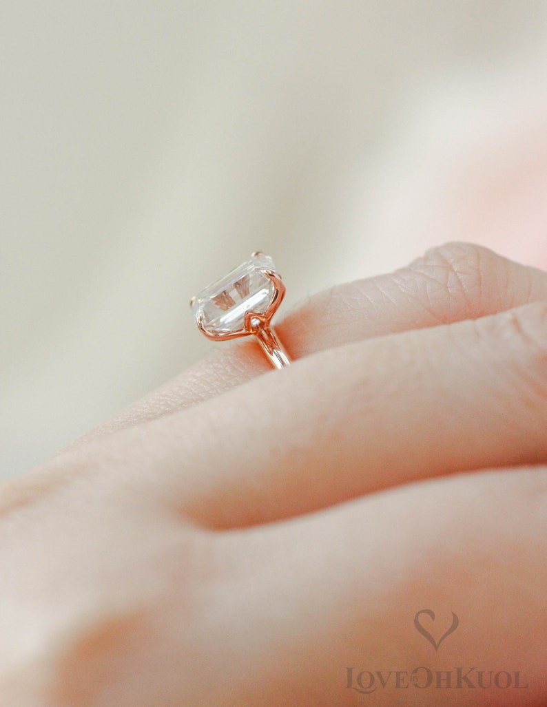 May include: A rose gold engagement ring with a large, clear, square-shaped diamond.