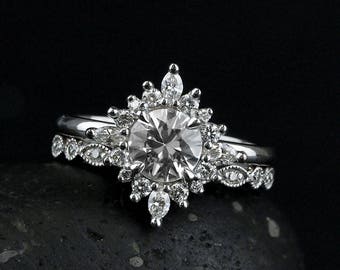 Puede incluir: Un anillo de compromiso de plata con una gran piedra central redonda rodeada por un halo de diamantes más pequeños. La banda es un diseño delicado de milgrain.