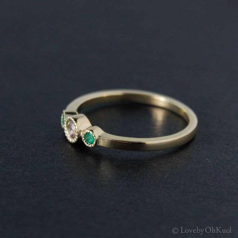 K&ouml;nnte beinhalten: Ein Goldring mit drei Steinen. Der mittlere Stein ist ein runder, klarer Stein, und die beiden Steine an den Seiten sind gr&uuml;n.