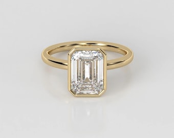May include: A gold engagement ring with a bezel-set emerald cut diamond.