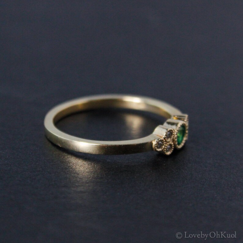 Pu&ograve; includere: Un anello d'oro con due pietre preziose verdi e pietre preziose trasparenti pi&ugrave; piccole incastonate in un grappolo.