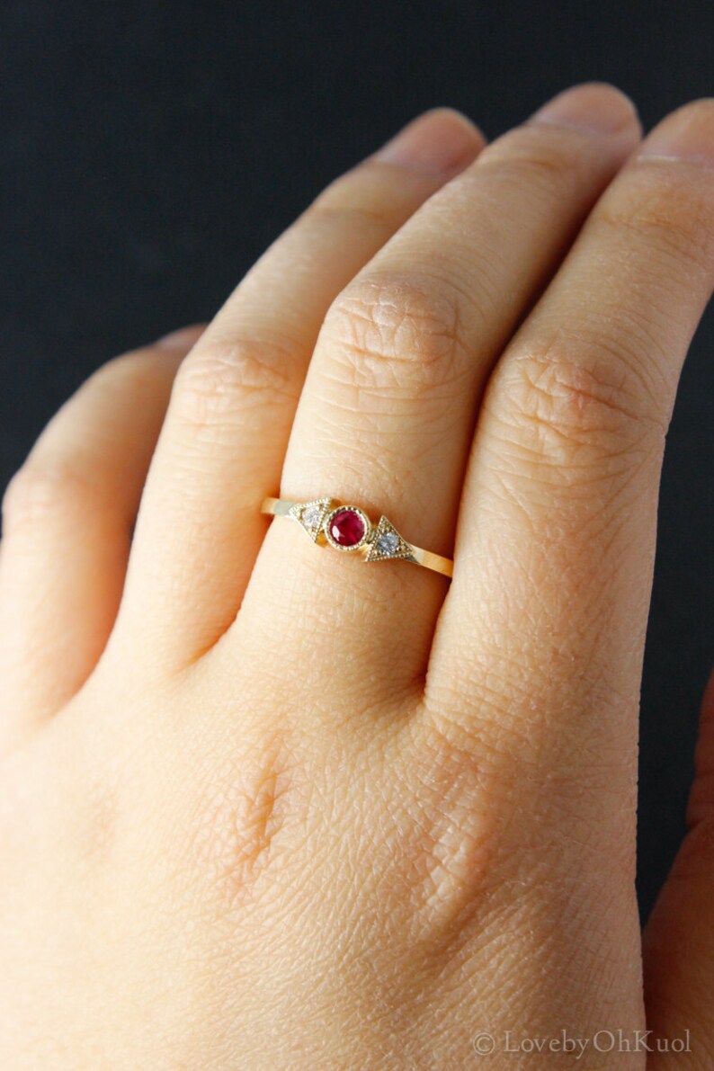 May include: A gold ring with a red gemstone and two smaller white gemstones set in a triangular shape.