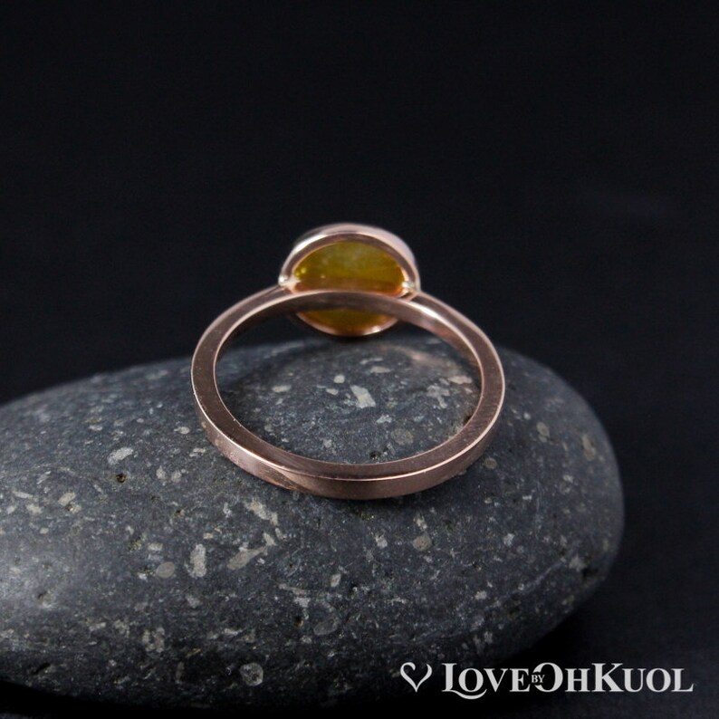 Puede incluir: Un anillo de oro rosa con una piedra ovalada amarilla. El anillo est&aacute; sobre una roca gris.