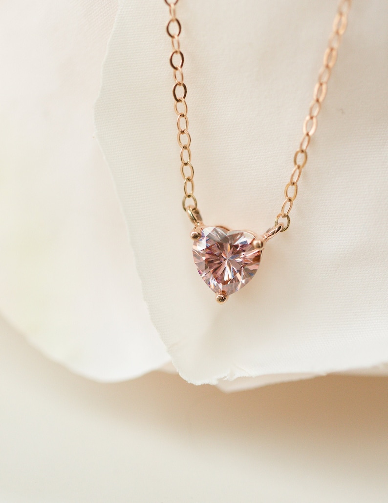 Puede incluir: Un delicado collar de cadena dorada con un colgante de coraz&oacute;n de piedra preciosa rosa.