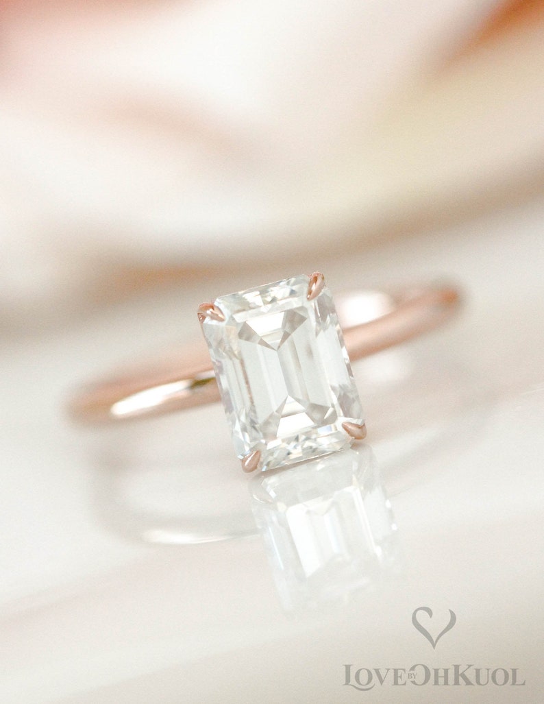 May include: A rose gold engagement ring with a large, clear emerald cut diamond.