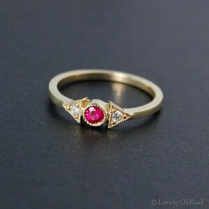 May include: A gold ring with a red ruby gemstone and two small diamonds set in triangular shapes.