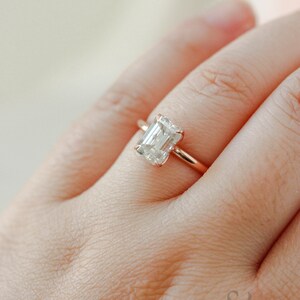 May include: A rose gold engagement ring with an emerald cut diamond.