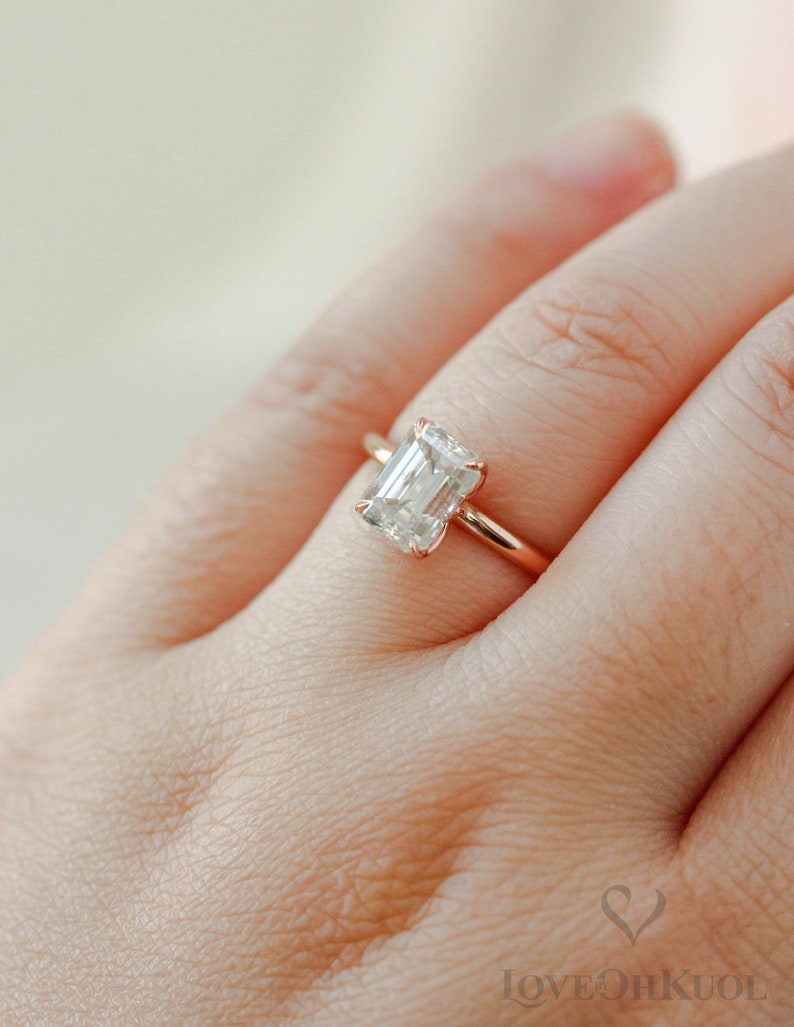 May include: A rose gold engagement ring with an emerald cut diamond.