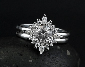 Puede incluir: Un anillo de compromiso de plata con una gran piedra central redonda rodeada de diamantes más pequeños en forma de estrella. El anillo está engastado en una banda doble.