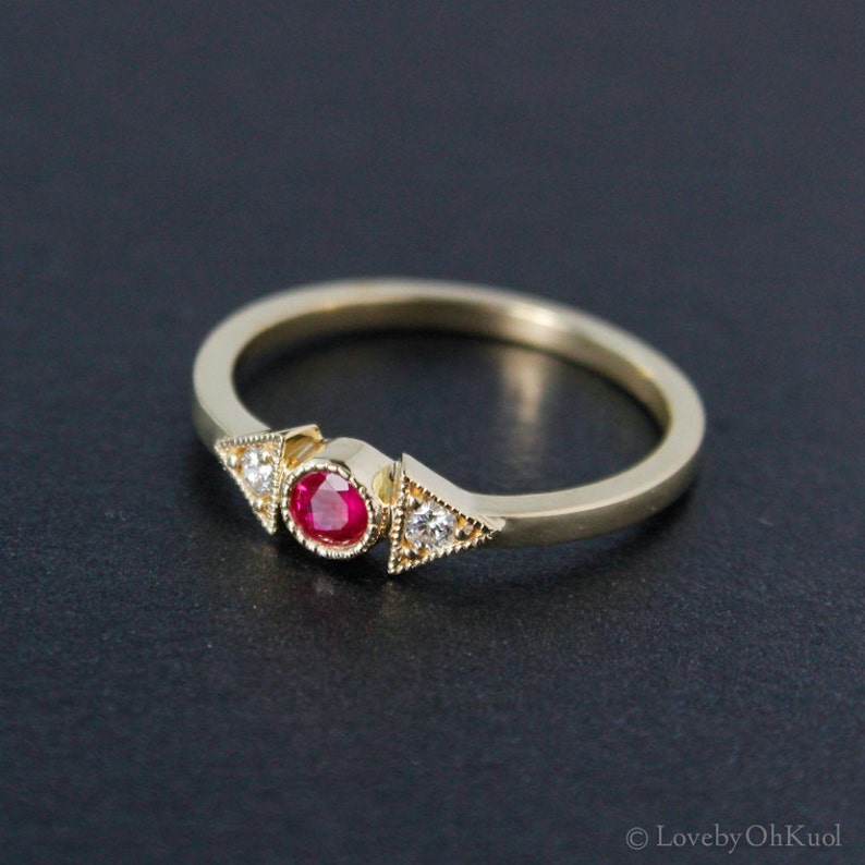 May include: A gold ring with a red ruby gemstone and two smaller white gemstones set in a triangular shape.