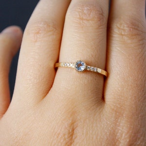 May include: A delicate gold ring with a light blue gemstone surrounded by small clear gemstones.