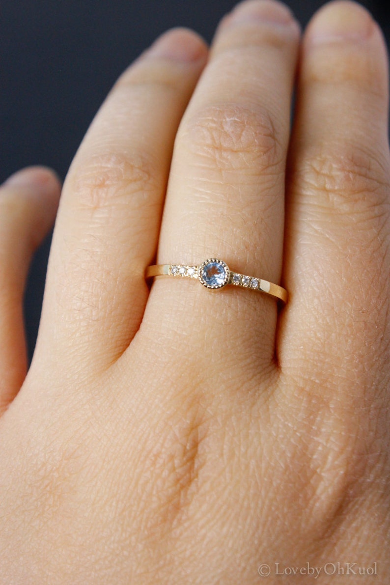 May include: A delicate gold ring with a light blue gemstone surrounded by small clear gemstones.