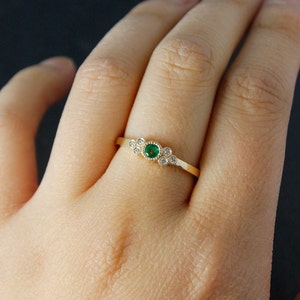 Pu&ograve; includere: Un anello d'oro con uno smeraldo verde circondato da diamanti pi&ugrave; piccoli.