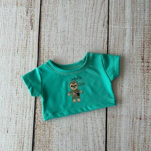May include: A teal-colored t-shirt with a graphic of a cartoon character and the words "Chewie and Chill". The shirt is made of a soft material and has short sleeves. The shirt is designed for a doll.