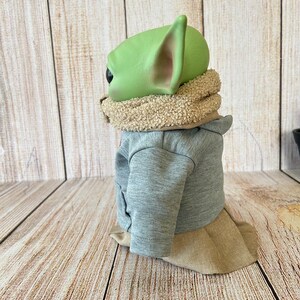May include: A green-skinned character with large ears, wearing a gray jacket, a tan scarf, and a tan skirt. The figure is a popular character from a science fiction franchise.
