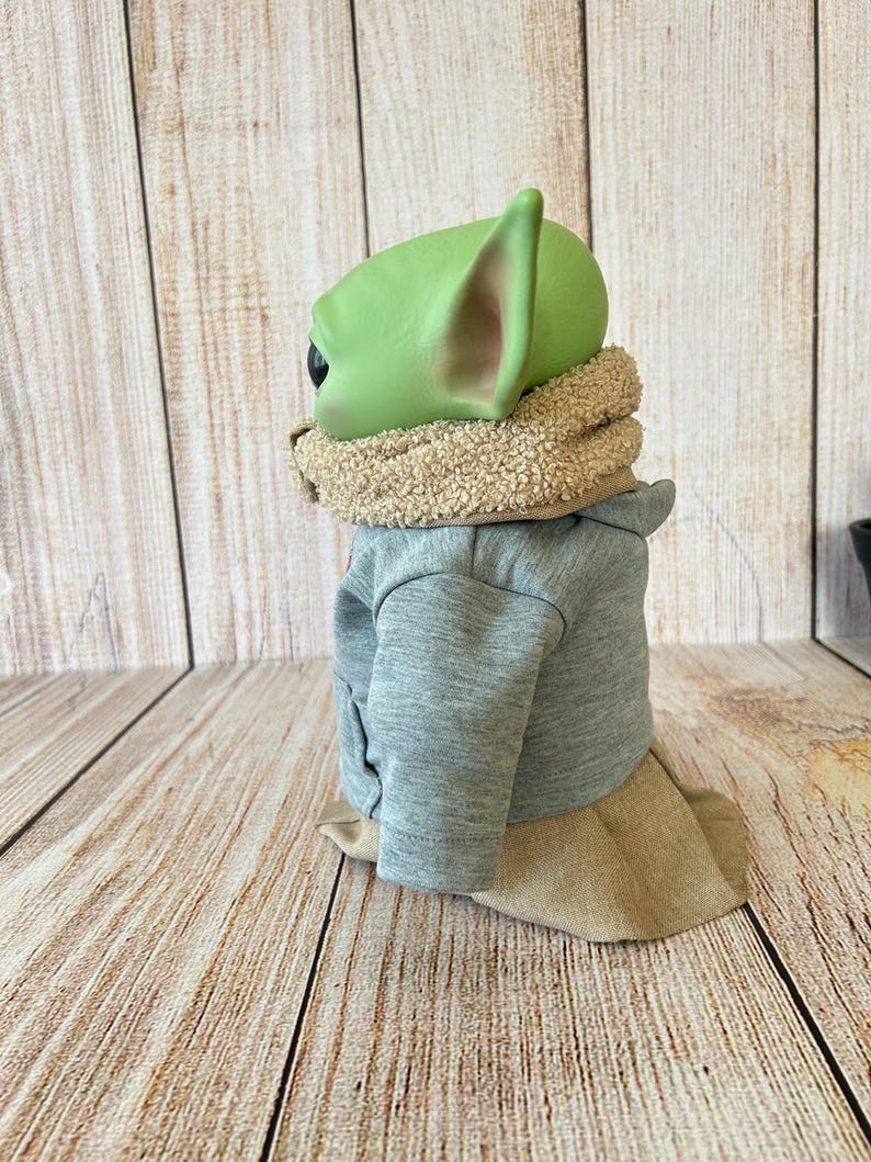 May include: A green-skinned character with large ears, wearing a gray jacket, a tan scarf, and a tan skirt. The figure is a popular character from a science fiction franchise.