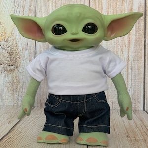 Puede incluir: Un juguete de peluche verde con orejas grandes, que lleva una camiseta blanca y pantalones cortos de mezclilla azul.