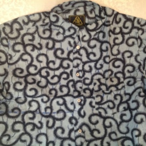 May include: A blue and black patterned short-sleeved button-up shirt with a triangular logo on the front.