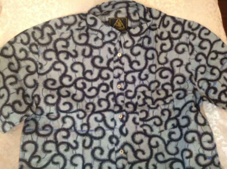 May include: A blue and black patterned short-sleeved button-up shirt with a triangular logo on the front.