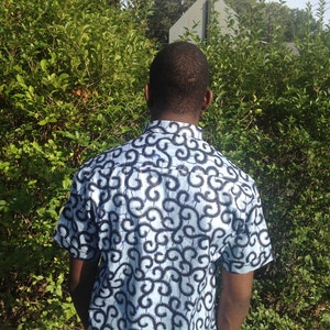 May include: A man wearing a short-sleeved shirt with a blue and black swirl pattern.