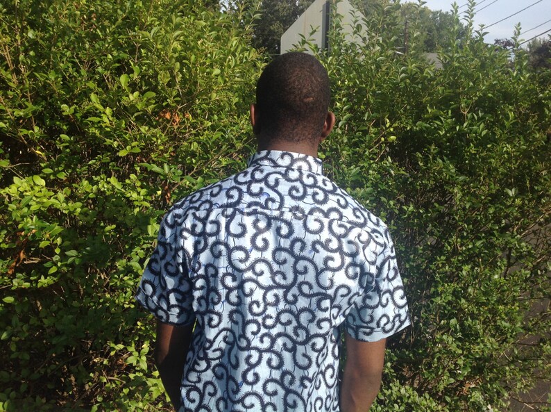 May include: A man wearing a short-sleeved shirt with a blue and black swirl pattern.