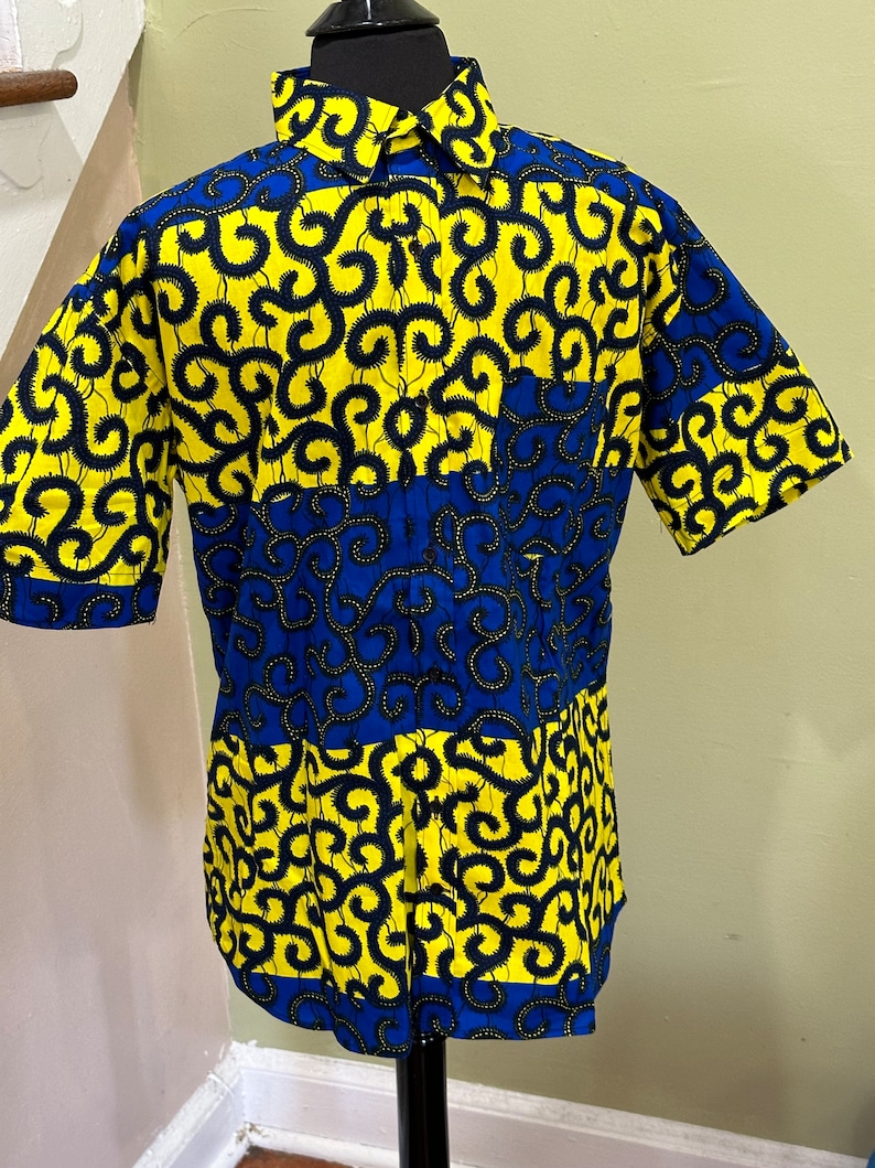 May include: A short-sleeved button-up shirt with a blue and yellow geometric pattern. The pattern features black swirls on a yellow background and blue swirls on a blue background.