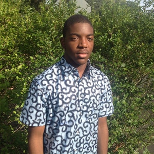 May include: A young person wearing a blue and black patterned short-sleeved shirt. The shirt has a button-up collar and a relaxed fit.