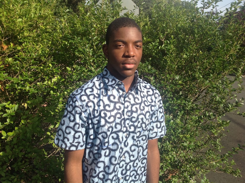 May include: A young person wearing a blue and black patterned short-sleeved shirt. The shirt has a button-up collar and a relaxed fit.