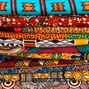 Puede incluir: Una pila de coloridas telas de estampados de cera africanos. Las telas presentan varios patrones, incluyendo formas geom&eacute;tricas, dise&ntilde;os florales y motivos abstractos. Los colores incluyen azul, rojo, naranja, amarillo y negro. Las telas est&aacute;n cuidadosamente dobladas, mostrando los diversos dise&ntilde;os.