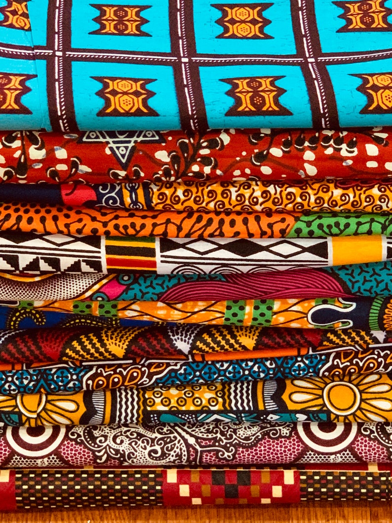 Puede incluir: Una pila de coloridas telas de estampados de cera africanos. Las telas presentan varios patrones, incluyendo formas geom&eacute;tricas, dise&ntilde;os florales y motivos abstractos. Los colores incluyen azul, rojo, naranja, amarillo y negro. Las telas est&aacute;n cuidadosamente dobladas, mostrando los diversos dise&ntilde;os.