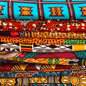 Puede incluir: Una pila de coloridas telas africanas estampadas con cera. Las telas muestran varios patrones, incluyendo formas geom&eacute;tricas, dise&ntilde;os florales y motivos abstractos. Los colores incluyen azul, naranja, rojo, amarillo y verde. Las telas est&aacute;n cuidadosamente dobladas, mostrando los diversos dise&ntilde;os.