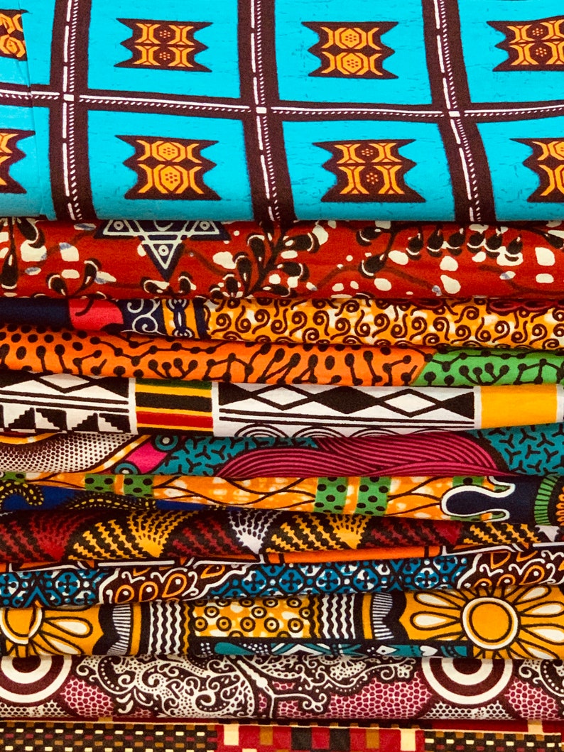 Puede incluir: Una pila de coloridas telas africanas estampadas con cera. Las telas muestran varios patrones, incluyendo formas geom&eacute;tricas, dise&ntilde;os florales y motivos abstractos. Los colores incluyen azul, naranja, rojo, amarillo y verde. Las telas est&aacute;n cuidadosamente dobladas, mostrando los diversos dise&ntilde;os.