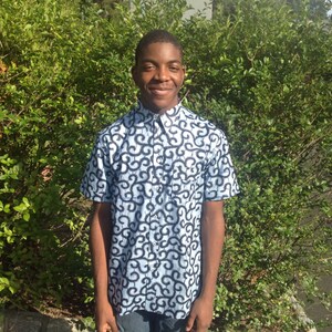 May include: A young person wearing a blue and black patterned short-sleeved shirt with a button-up collar.