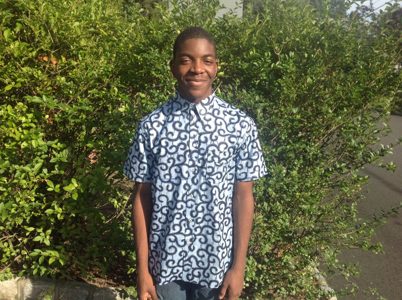 May include: A young person wearing a blue and black patterned short-sleeved shirt with a button-up collar.