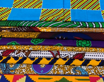 May include: A stack of colorful fabric with various patterns, including a blue and yellow checkered pattern, a purple and yellow floral pattern, and a yellow and red geometric pattern.