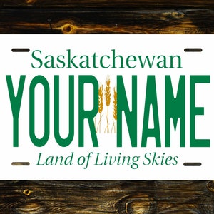 May include: A white Saskatchewan licence plate with green text that reads "Saskatchewan" and "YOUR NAME" with a graphic of wheat stalks. The bottom of the plate reads "Land of Living Skies".