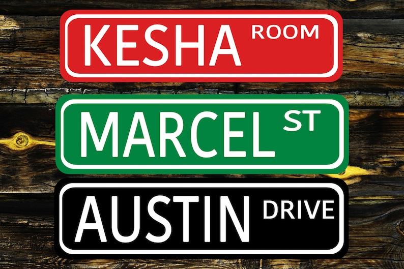 May include: Three personalized street signs with white lettering on a colored background. The top sign is red with "Kesha Room" written on it. The middle sign is green with "Marcel St" written on it. The bottom sign is black with "Austin Drive" written on it.