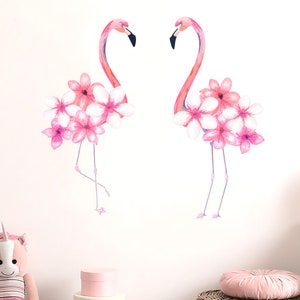 May include: Two pink flamingos with pink flowers on their backs. The flamingos are standing on a white background.