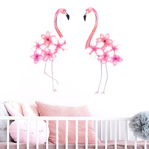 May include: Two pink flamingos with pink flowers on their heads, against a white background. The flamingos are facing each other.