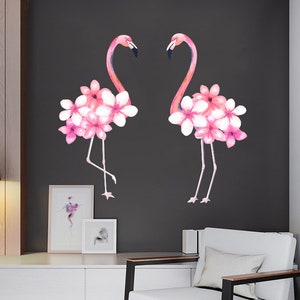 May include: Two pink flamingos with pink flowers on their necks, against a dark grey background.