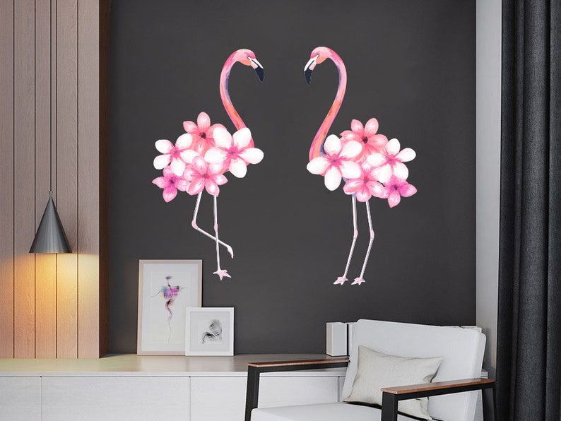 May include: Two pink flamingos with pink flowers on their necks, against a dark grey background.