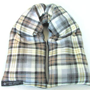 May include: A plaid fabric neck wrap filled with rice for heat therapy. The wrap is beige, brown, and gray with a black label that reads "Divine Comfort: Rice Packs".