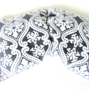 Puede incluir: Una envoltura para el cuello con estampado gris y blanco. La tela presenta un dise&ntilde;o de damasco con elementos florales y punteados. La envoltura est&aacute; doblada en forma de V.