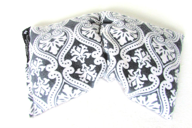 Puede incluir: Una envoltura para el cuello con estampado gris y blanco. La tela presenta un dise&ntilde;o de damasco con elementos florales y punteados. La envoltura est&aacute; doblada en forma de V.