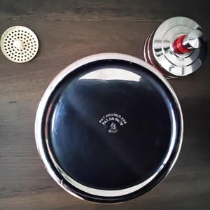 May include: A set of three chrome kitchen accessories. The set includes a round, perforated strainer, a lid with a red accent, and a large, shiny bowl with the text "PAT.NO.969.388 PAT.NO.94.78". The bowl has a black interior and a silver rim.