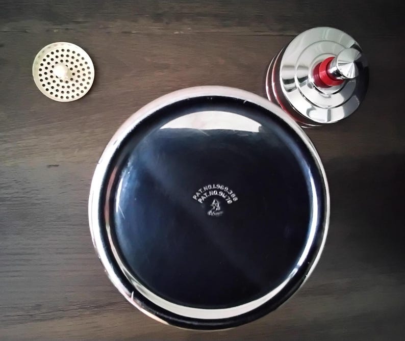 May include: A set of three chrome kitchen accessories. The set includes a round, perforated strainer, a lid with a red accent, and a large, shiny bowl with the text "PAT.NO.969.388 PAT.NO.94.78". The bowl has a black interior and a silver rim.